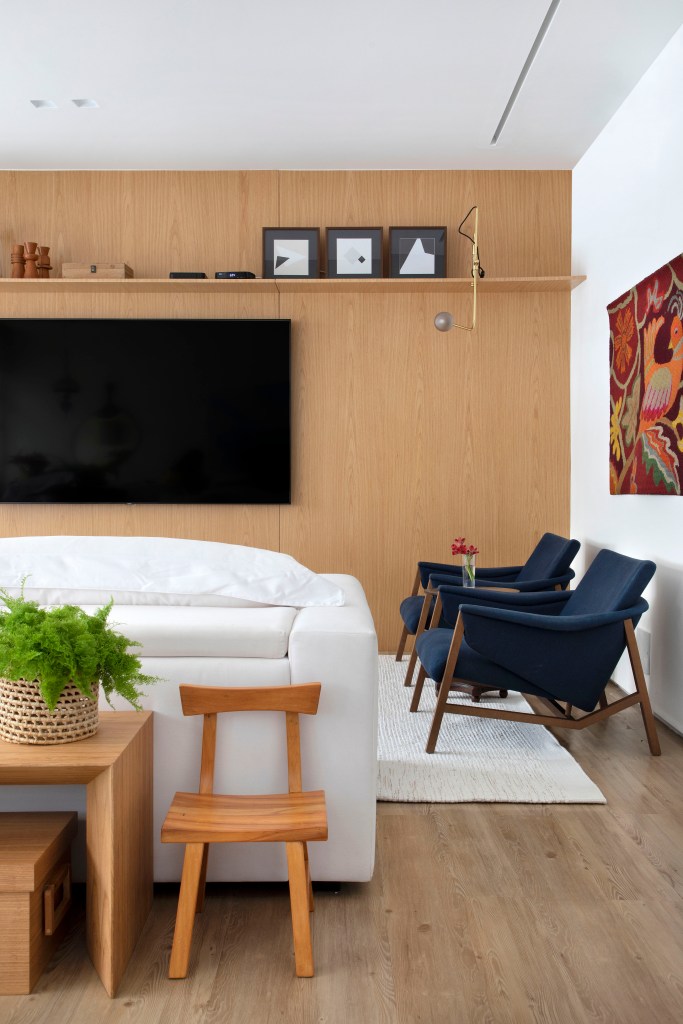 Sala de tv com sofá branco e parede revestida em madeira