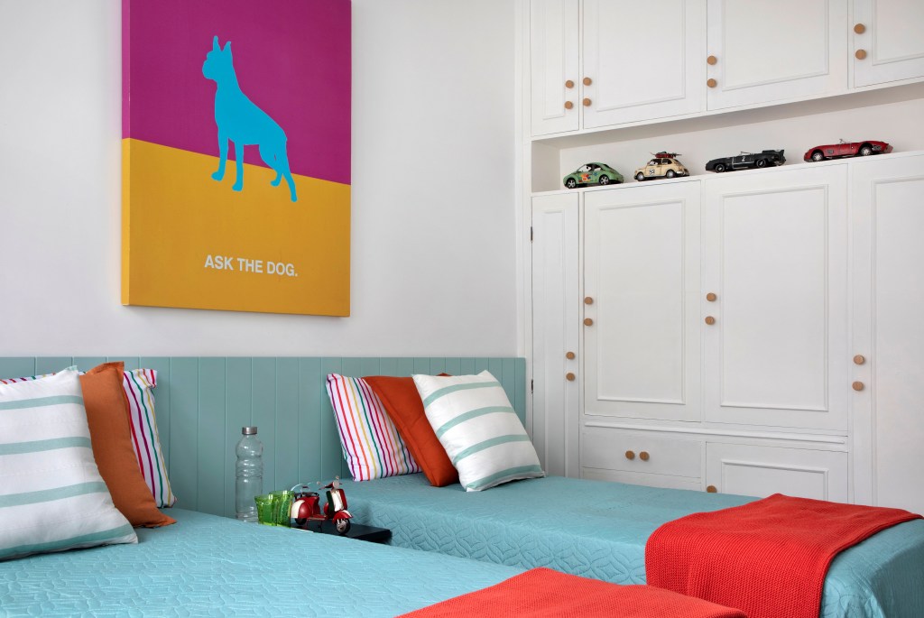 Quarto com duas camas, armário branco e quadro colorido