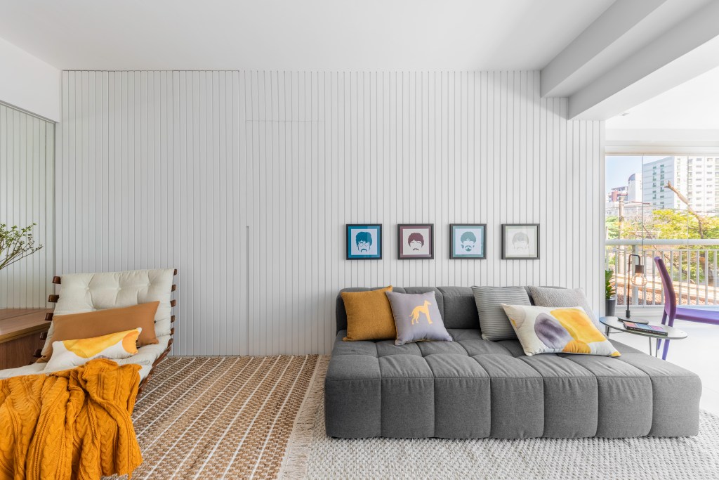 Sala com parede em madeira ripada; sofá baixo; quadros dos Beatles acima do sofá