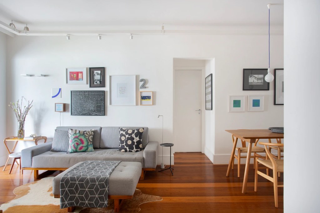 Sala de estar com sofá cinza; sala de estar integrada com jantar; quadros na parede.