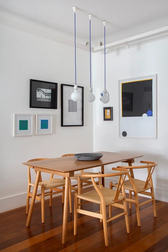 Sala de jantar; mesa em madeira; luminária; quadros na parede.