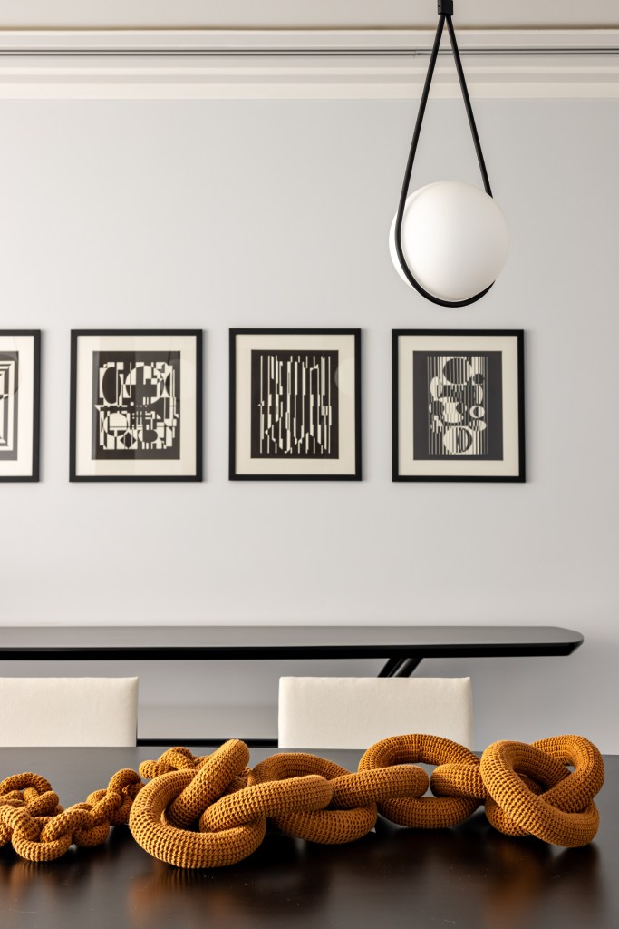 Sala de jantar; mesa preta; cadeiras pretas e brancas; luminárias esféricas com suporte metálico em forma de gota; quadros na parede