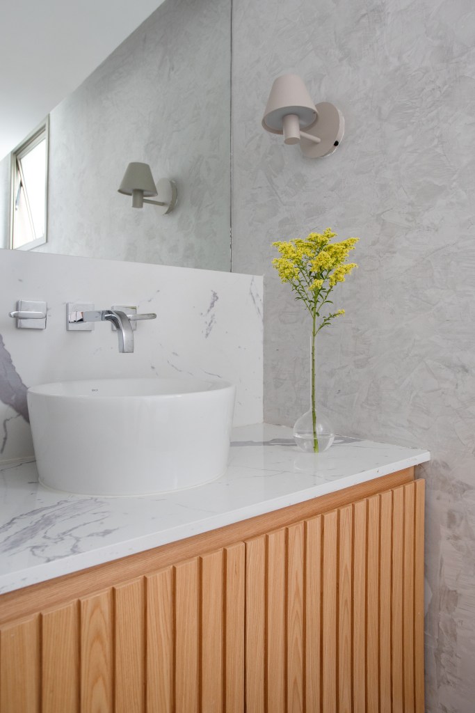 Banheiro com bancada de mármore; armário de madeira; cuba solta.