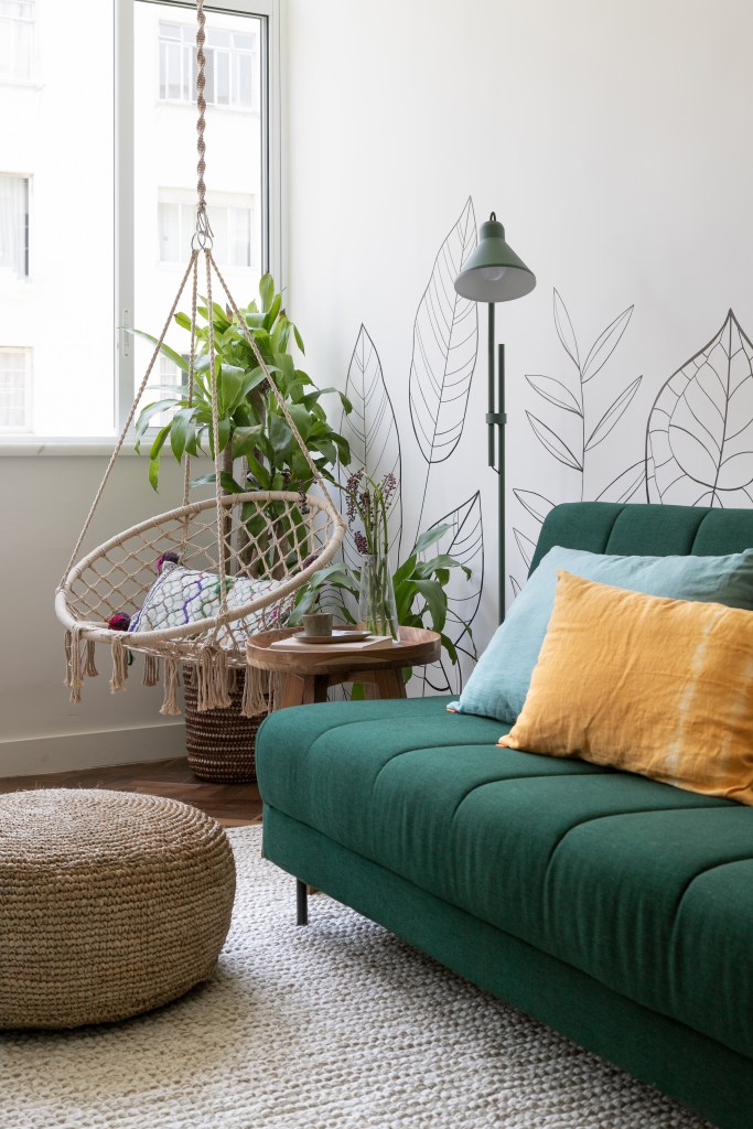 Sala de estar com sofá verde; balanço de macramê; luminária de piso.