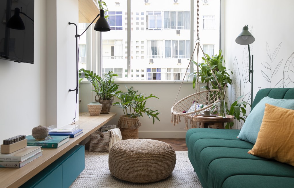 Sala pequena com sofá verde; pufe; plantas; tv
