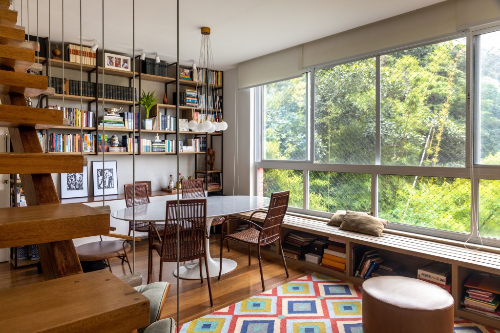 Sala com escada; biblioteca; tapete colorido; poltrona Eames; mesa de jantar