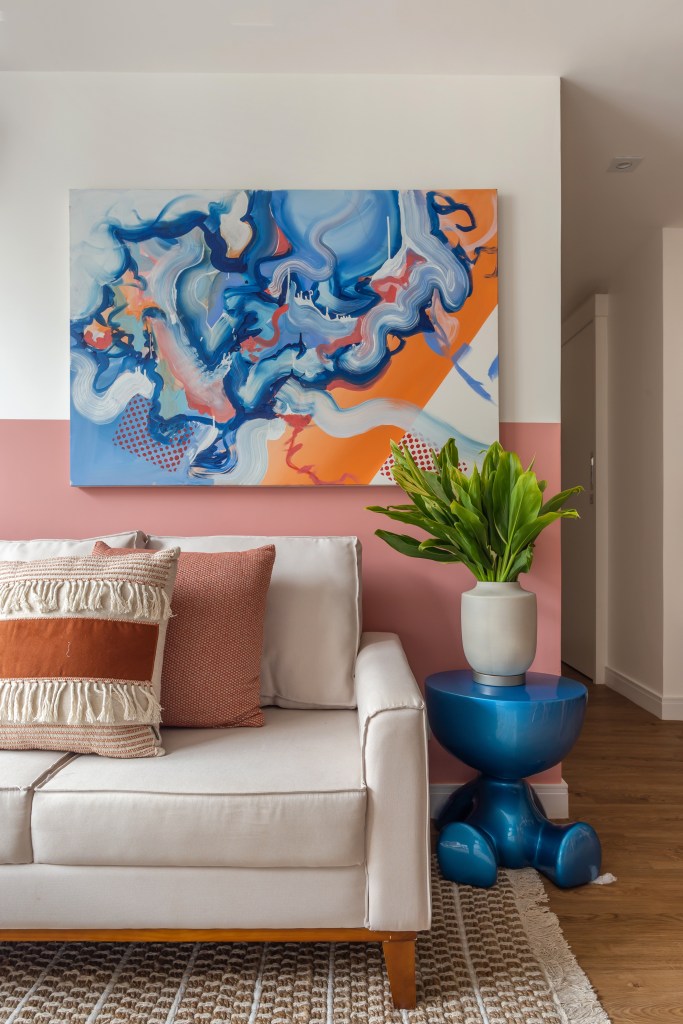 Sala de estar com sofá branco; meia parede rosa; quadro cima do sofá