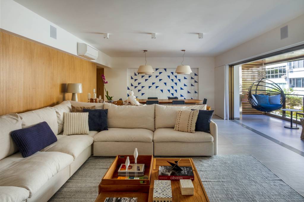 Sala de estar com sofá em L branco e painel de azulejos ao fundo