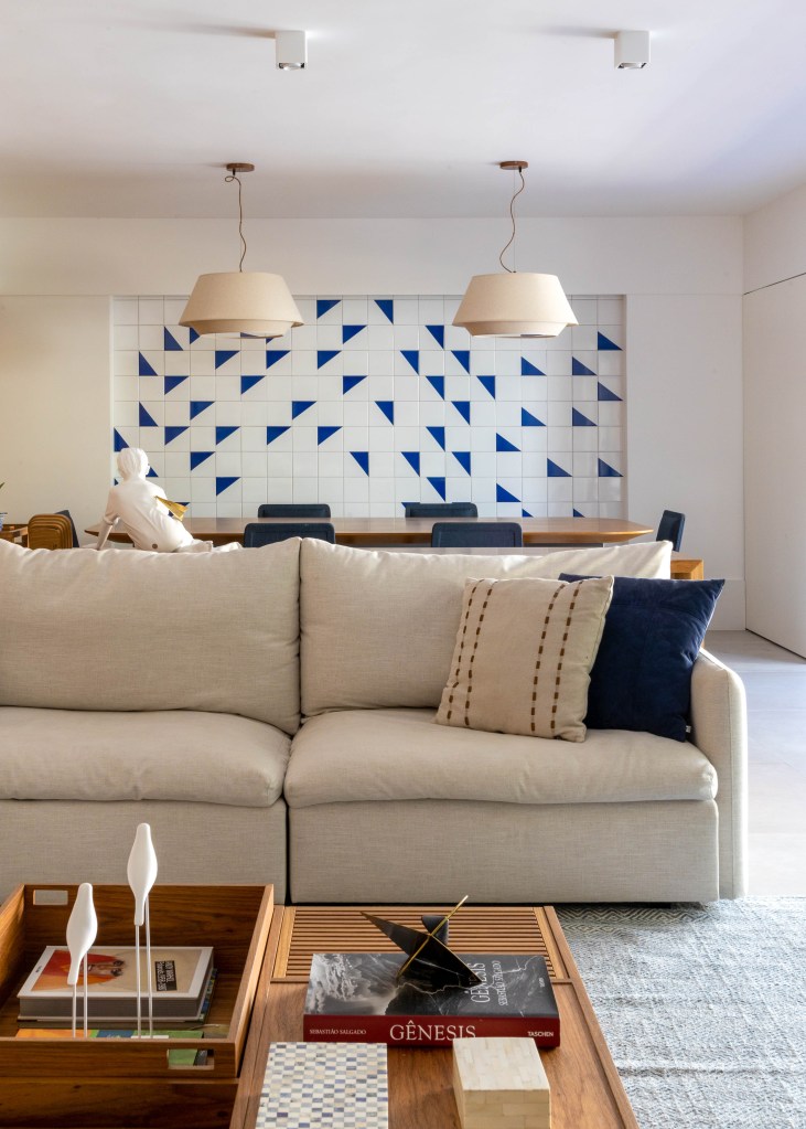Sala de estar com sofá em L branco e painel de azulejos ao fundo