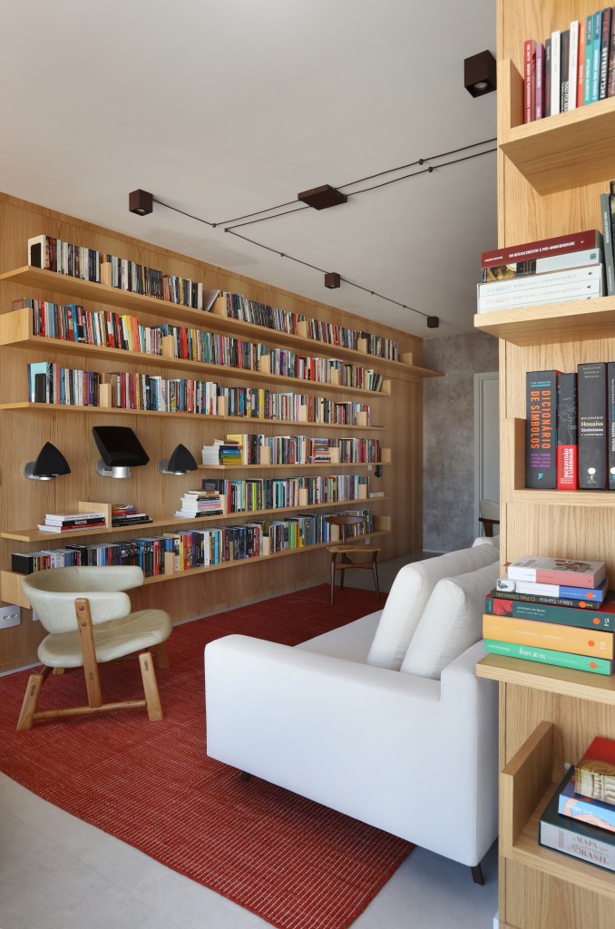 Sala de estar; estante; livros; poltrona; sofá branco; tapete vermelho