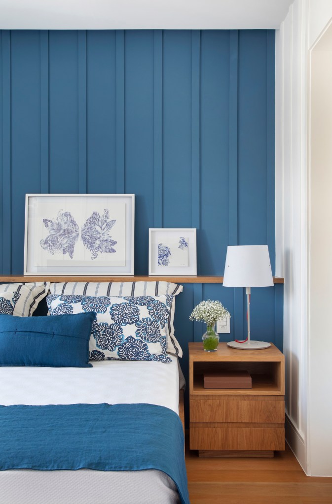 Quarto com parede azul; roupa de cama azul; mesinha lateral de madeira