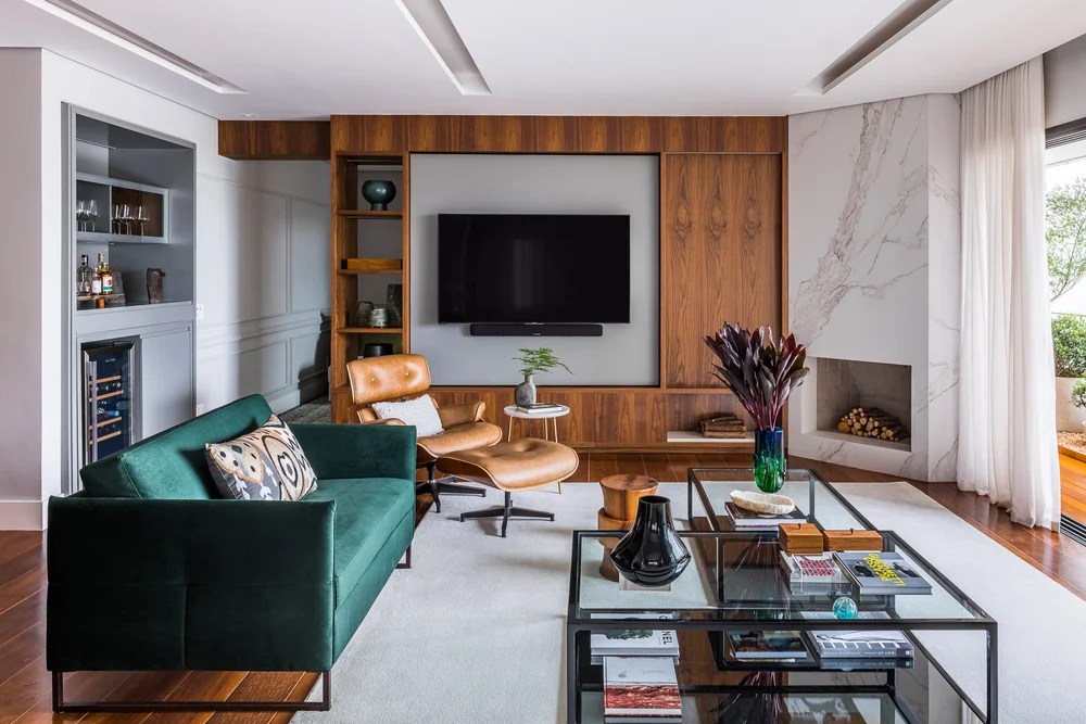 Sala de tv; estante de madeira; sofá verde; poltrona eames lounge; tapete; mesa de centro de vidro