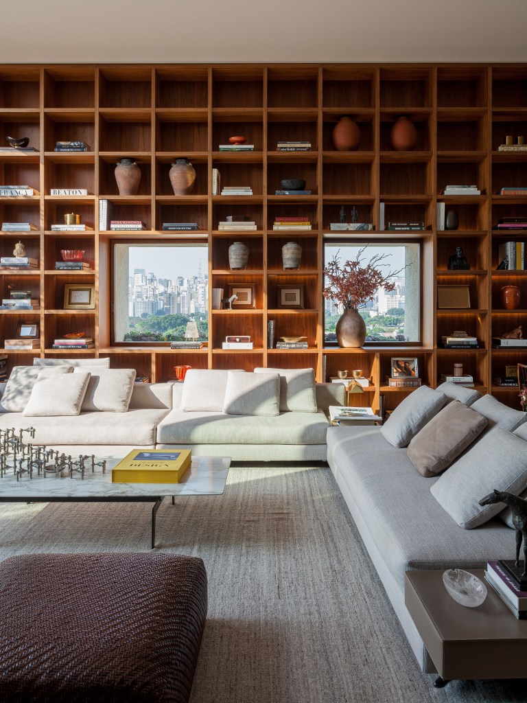 Sala de estar; estante de madeira com nichos; sofás cinza; marcenaria; pufe de couro