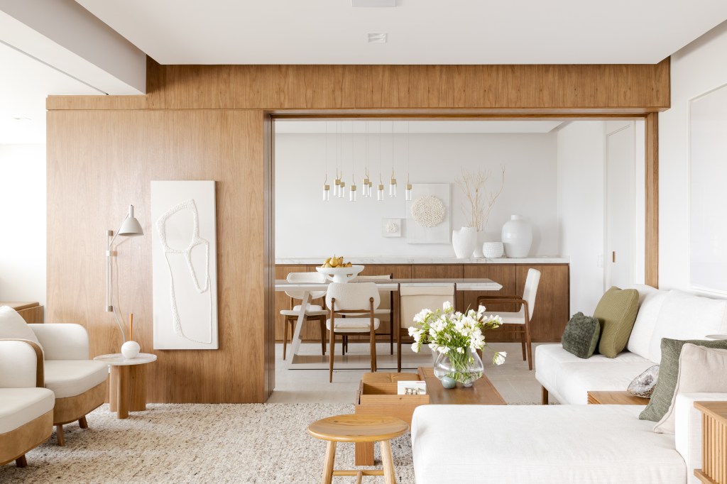 Sala de estar; poltrona branca; tapete; madeira; porta de correr de madeira; mesa de centro; sala de jantar