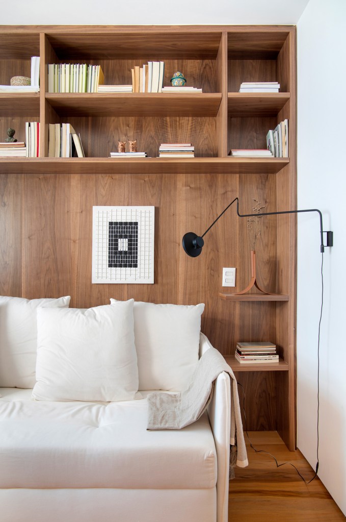 Quarto; sofá branco; cantinho de leitura; estante de madeira; luminária de parede