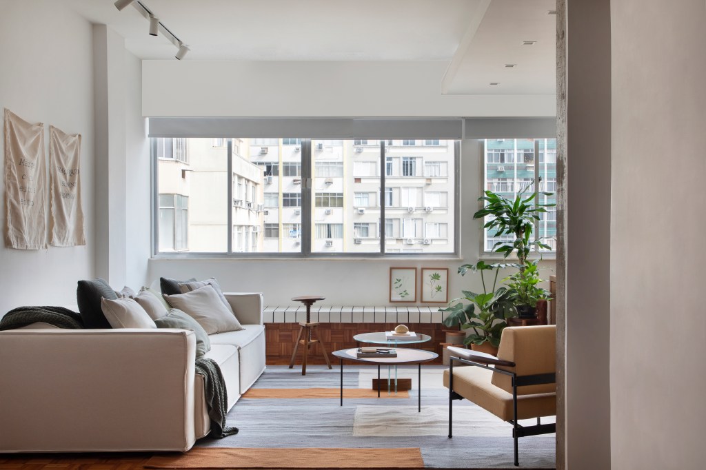 Sala de estar; sofá branco; banco de madeira com azulejos; janela; plantas