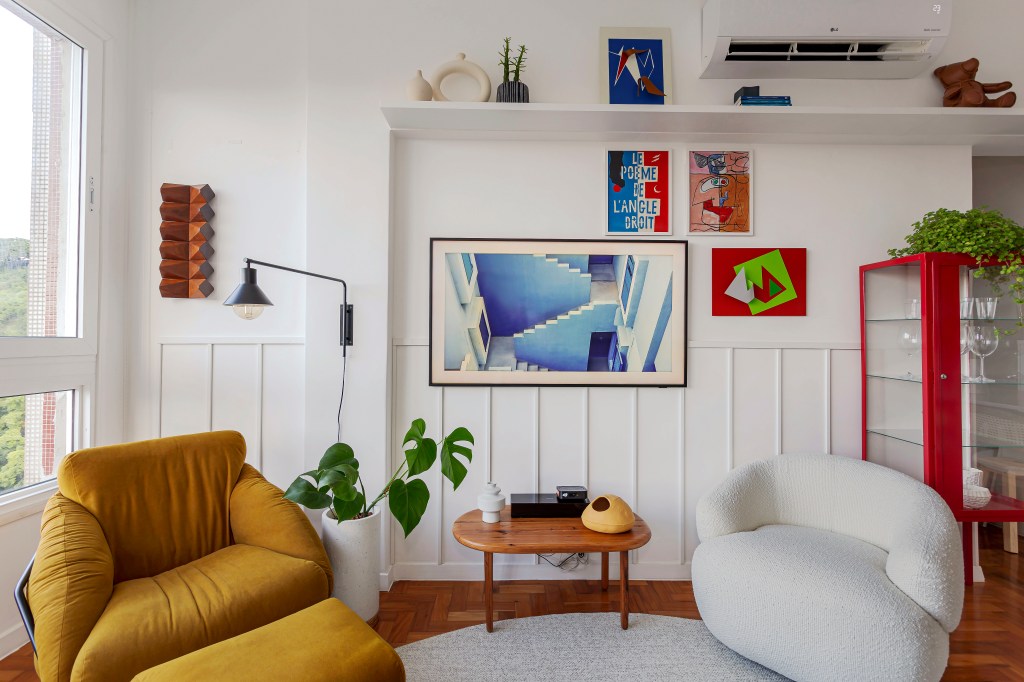 Sala de estar; poltrona branca; poltrona mostarda; quadros; boiserie; luminária de parede