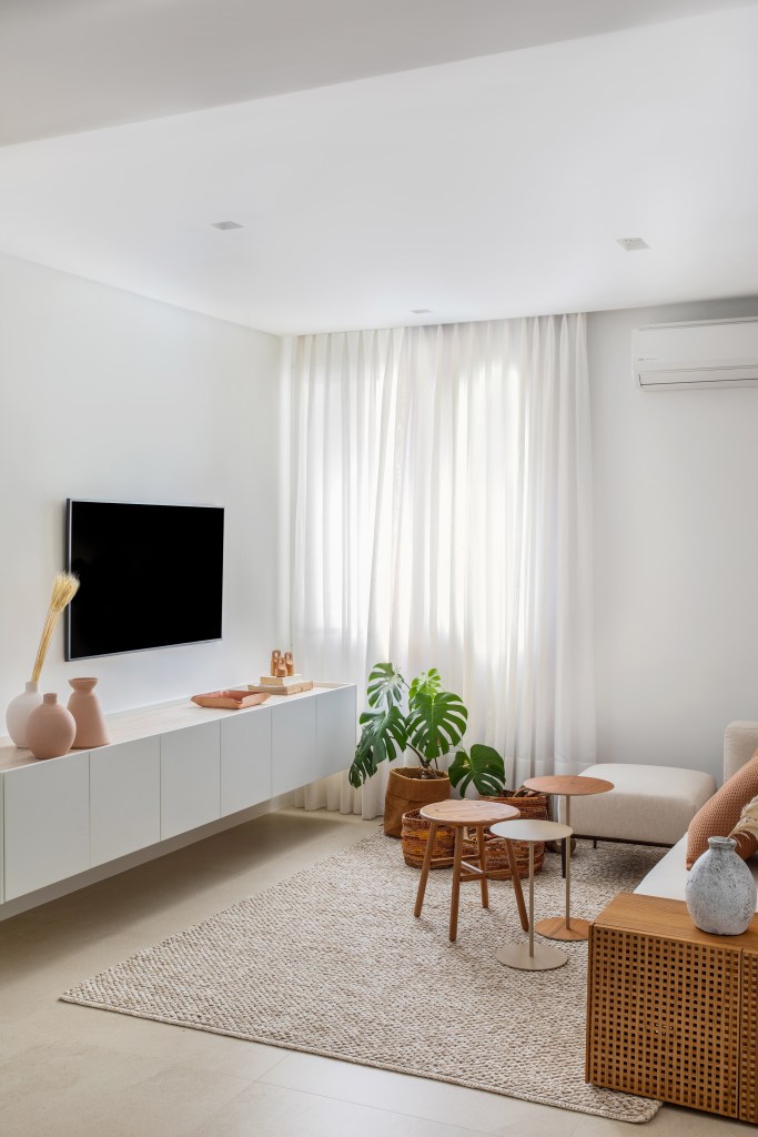 Sala; sala de tv; tapete bege; sofá branco; mesa de centro de madeira; plantas; rack branco; cortina branca