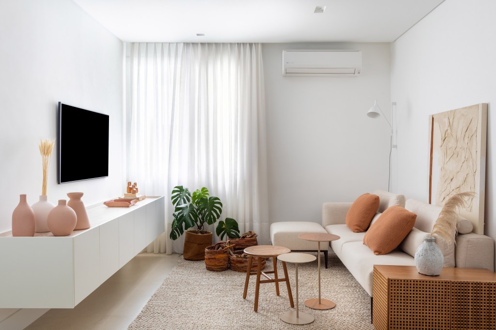 Sala; sala de tv; tapete bege; sofá branco; mesa de centro de madeira; plantas; rack branco; cortina branca