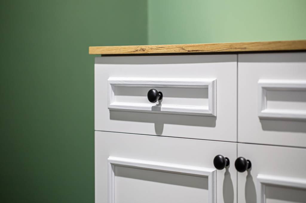 Close-up of a white cabinet with black handles on a green wall background. Faça você mesmo: 4 formas de repaginar os armários sozinho