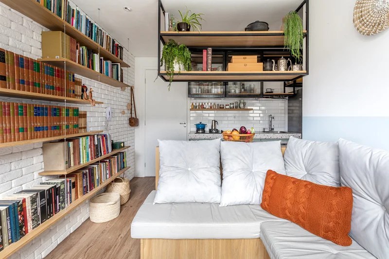 Cozinha integrada; cozinha pequena; apartamento pequeno; cozinha americana; cozinha integrada com sala; estante de livros; sofá de madeira; almofada branca