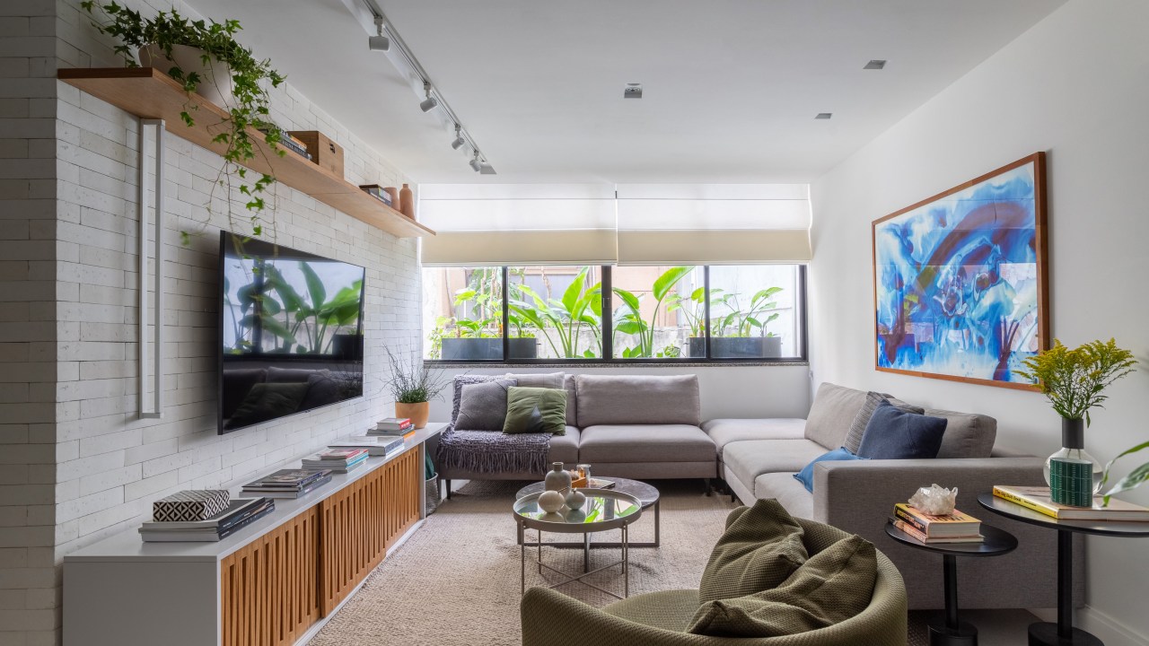 Sala de estar; sala de tv; parede de tijolinho branco; sofá cinza; tapete; mesa de centro; poltrona verde