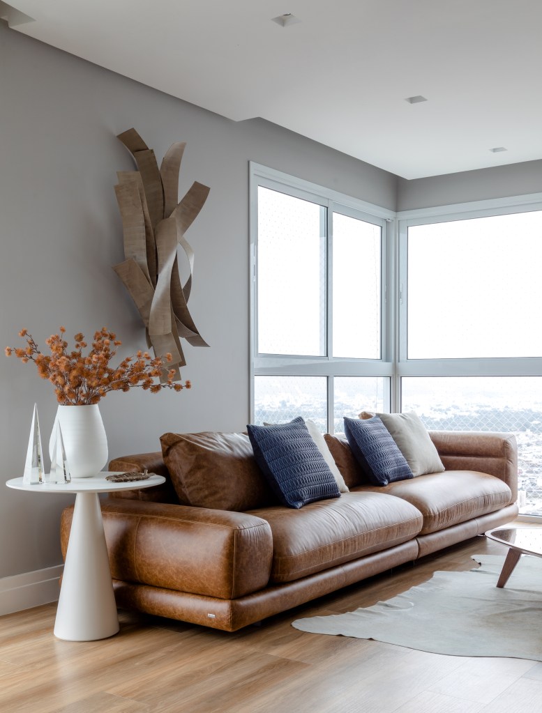 Piso vinílico; sala de estar; escultura de parede; sofá de couro marrom; mesa lateral