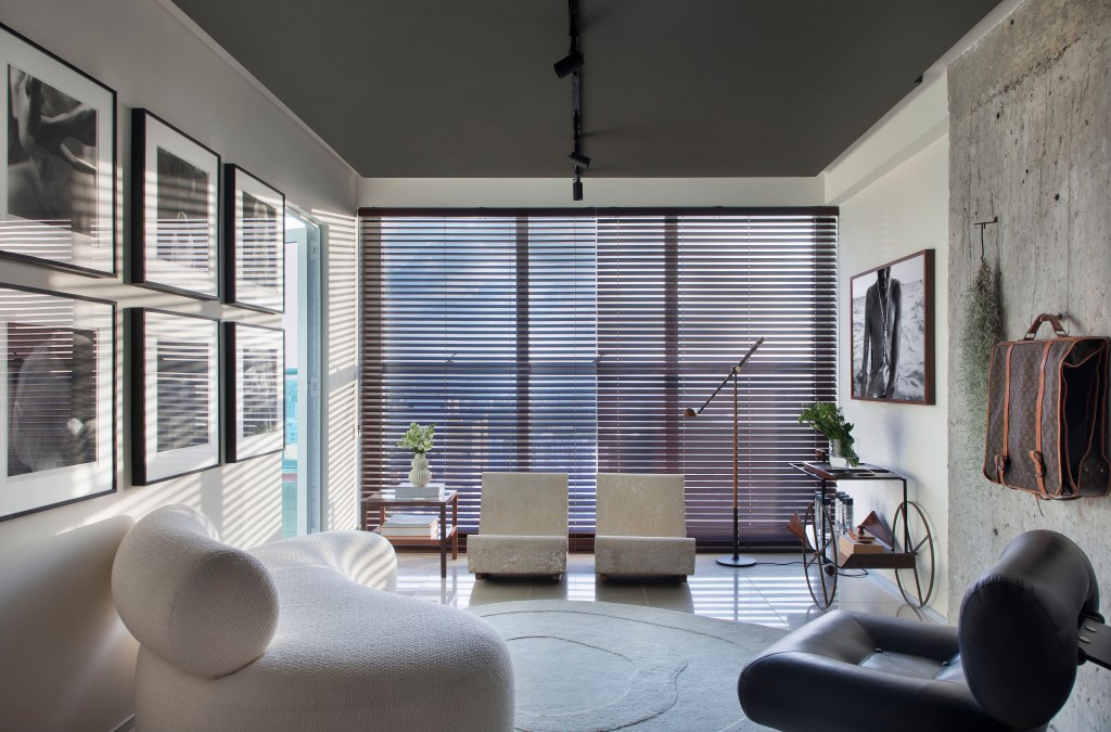 Sala de estar; paleta sóbria; parede de concreto; piso de porcelanato; tapete; persiana