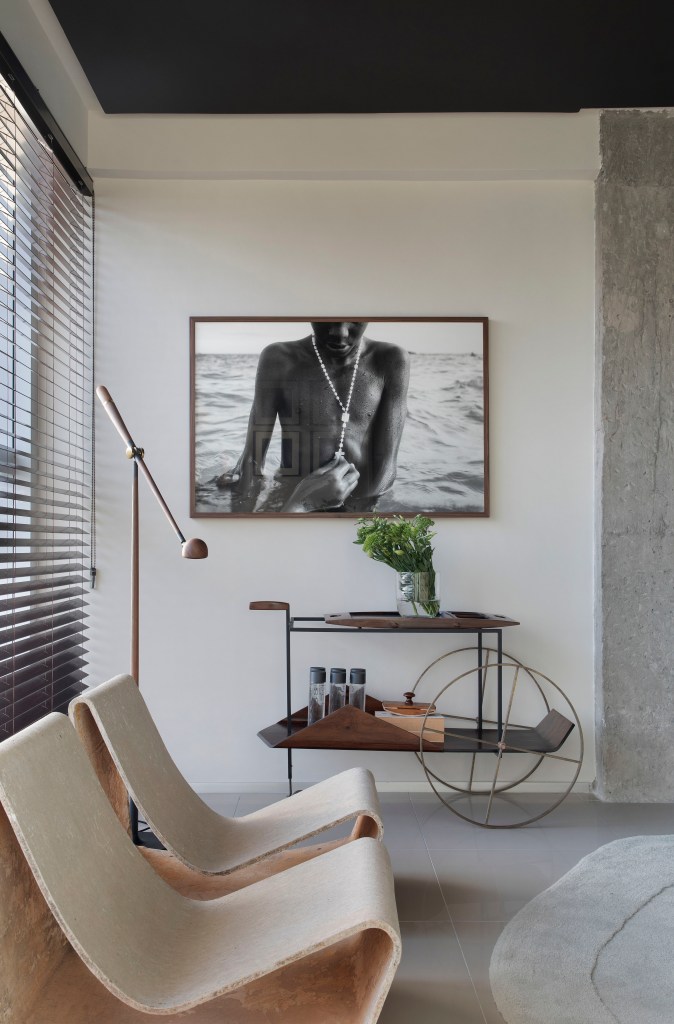 Sala de estar; paleta sóbria; parede de concreto; foto; luminária de piso; carrinho de chá; poltrona branca