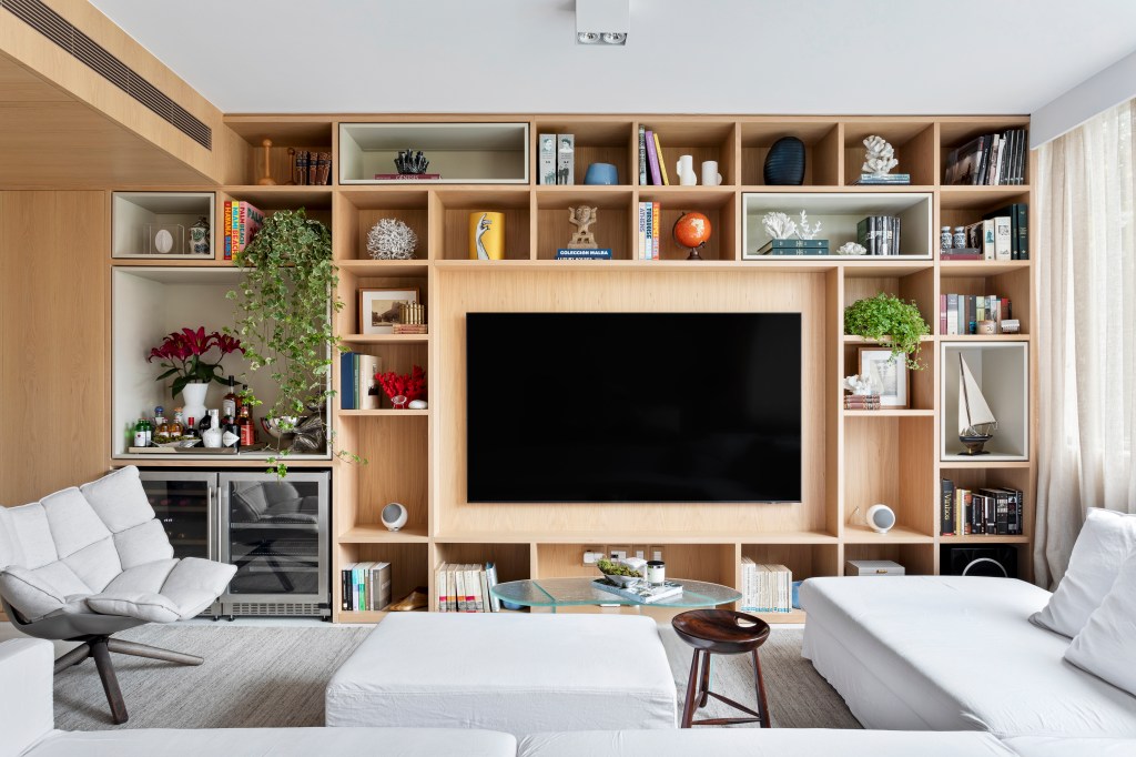 Sala de estar; sala de tv com estante de nichos em madeira; tapete claro; poltrona e sofás brancos;