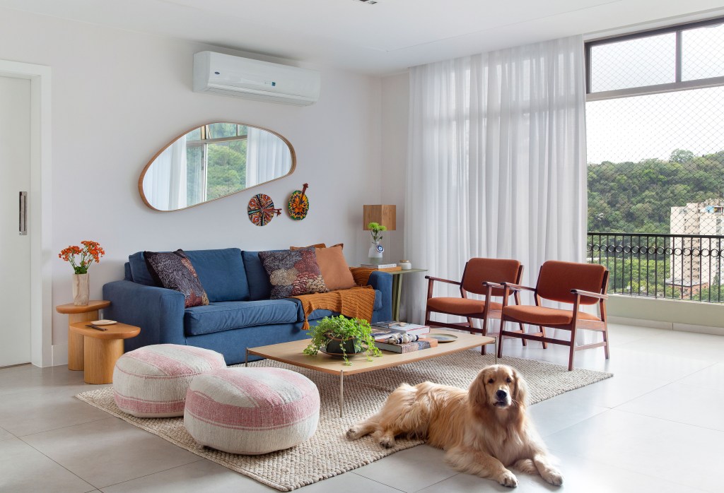 Sala de estar; sofá azul; poltrona; pufe; mesa de centro; tapete; cortina branca; ar condicionado; espelho; espelho orgânico