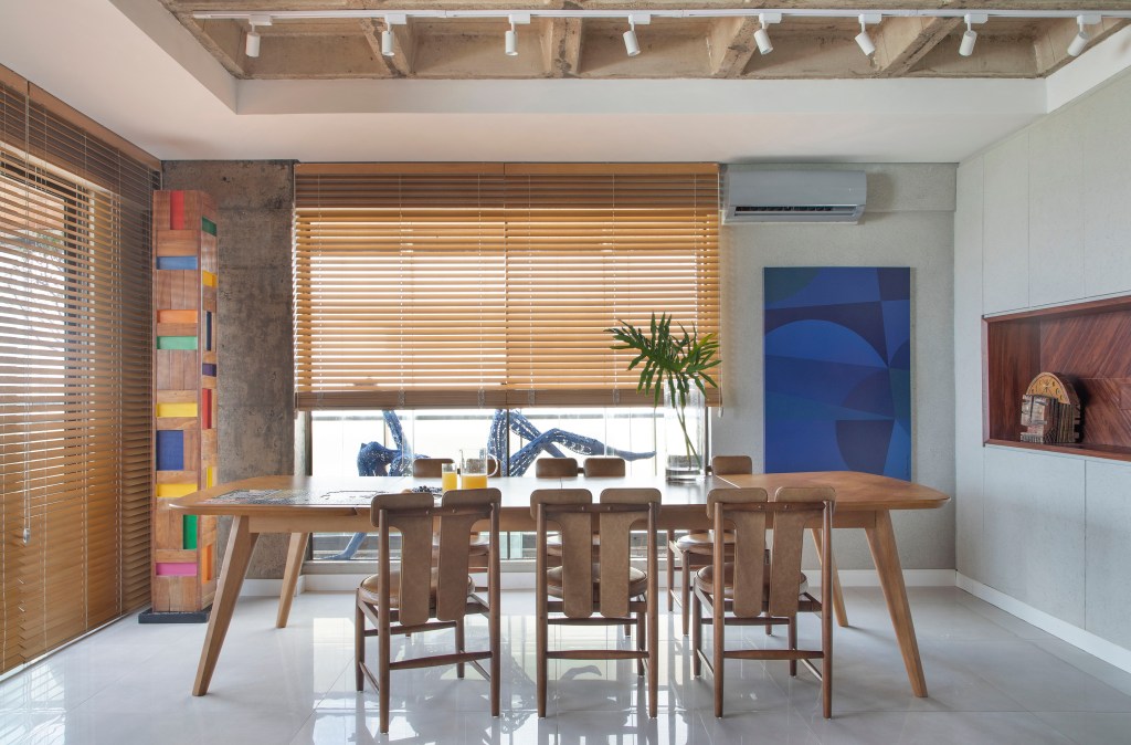 Sala de jantar com mesa e cadeiras de madeira; quadro azul na parede