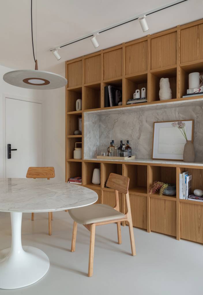 Sala de jantar com paredes brancas, mesa redonda com tampo branco, cadeiras de madeira e estante de madeira