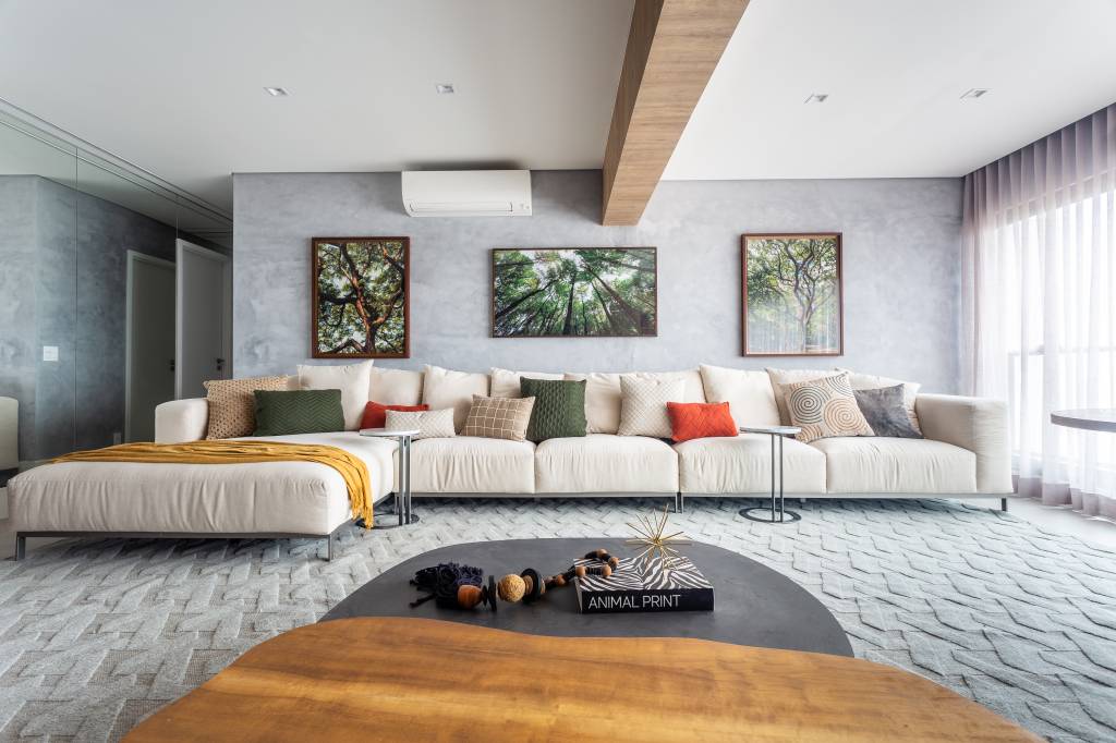 Sala de estar com sofá branco grande, parede de cimento queimado e fotografias de árvores.