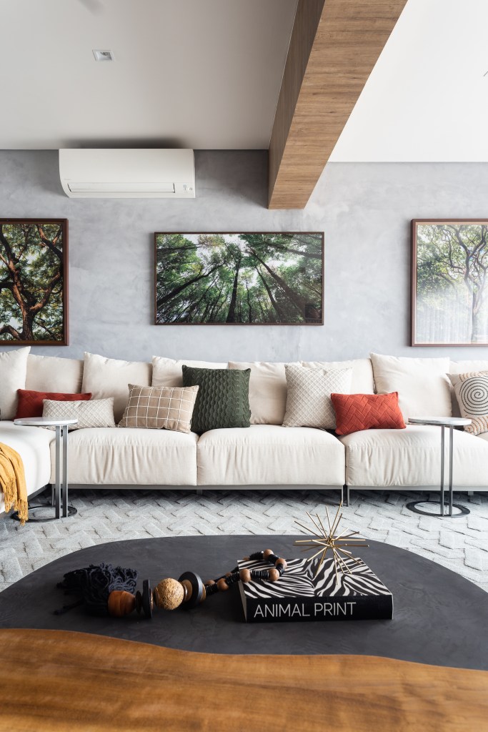 Sala de estar com sofá branco grande, parede de cimento queimado e fotografias de árvores.