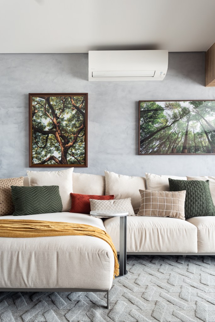 Sala de estar com sofá branco grande, parede de cimento queimado e fotografias de árvores.