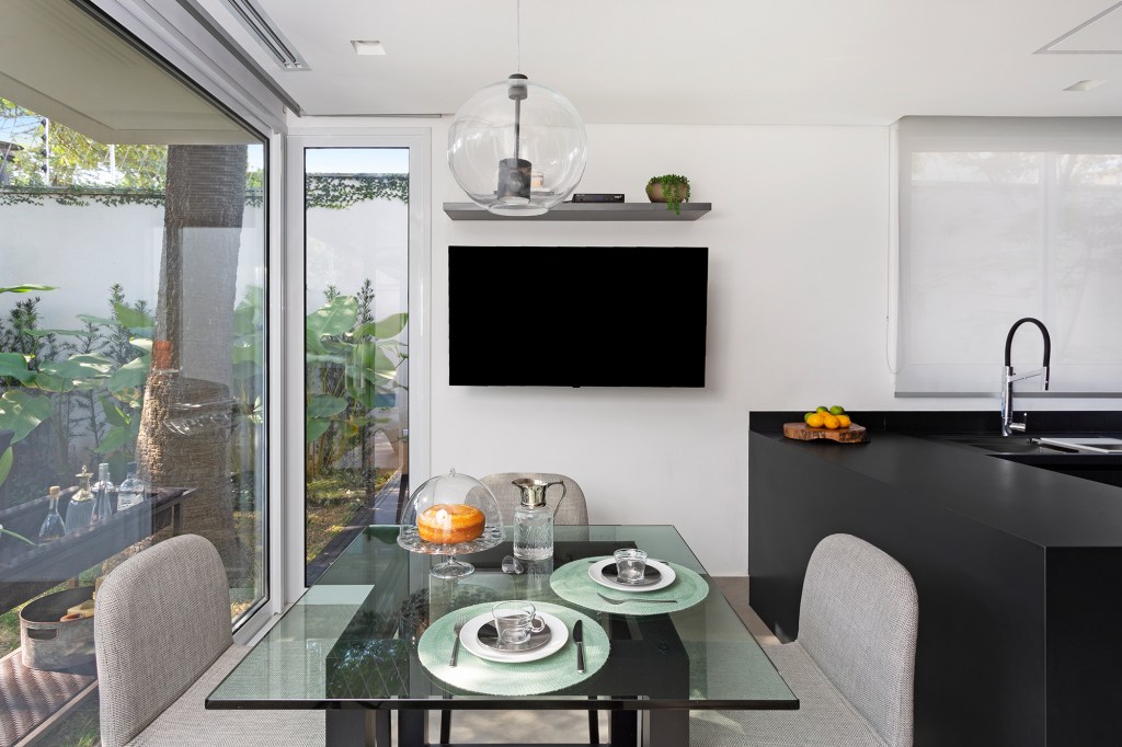 Casa 290 m² ganha cozinha preta com vista para jardim tropical Cadda Arquitetura decoração Carolina Haddad bancada mesa cadeira jantar tv