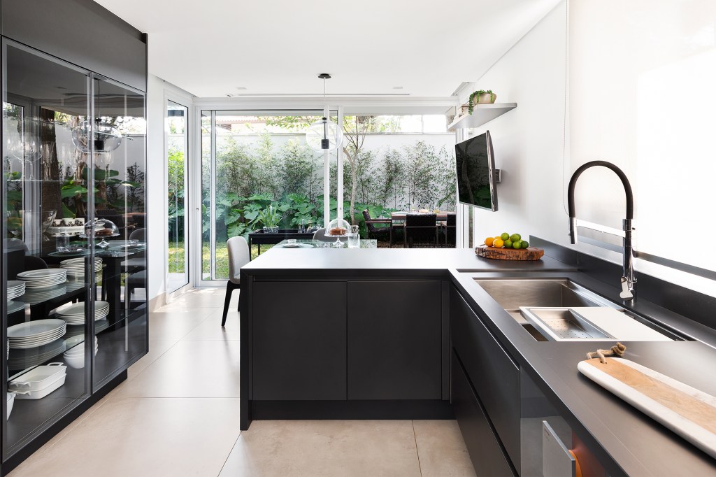 Casa 290 m² ganha cozinha preta com vista para jardim tropical Cadda Arquitetura decoração Carolina Haddad armario bancada cristaleira