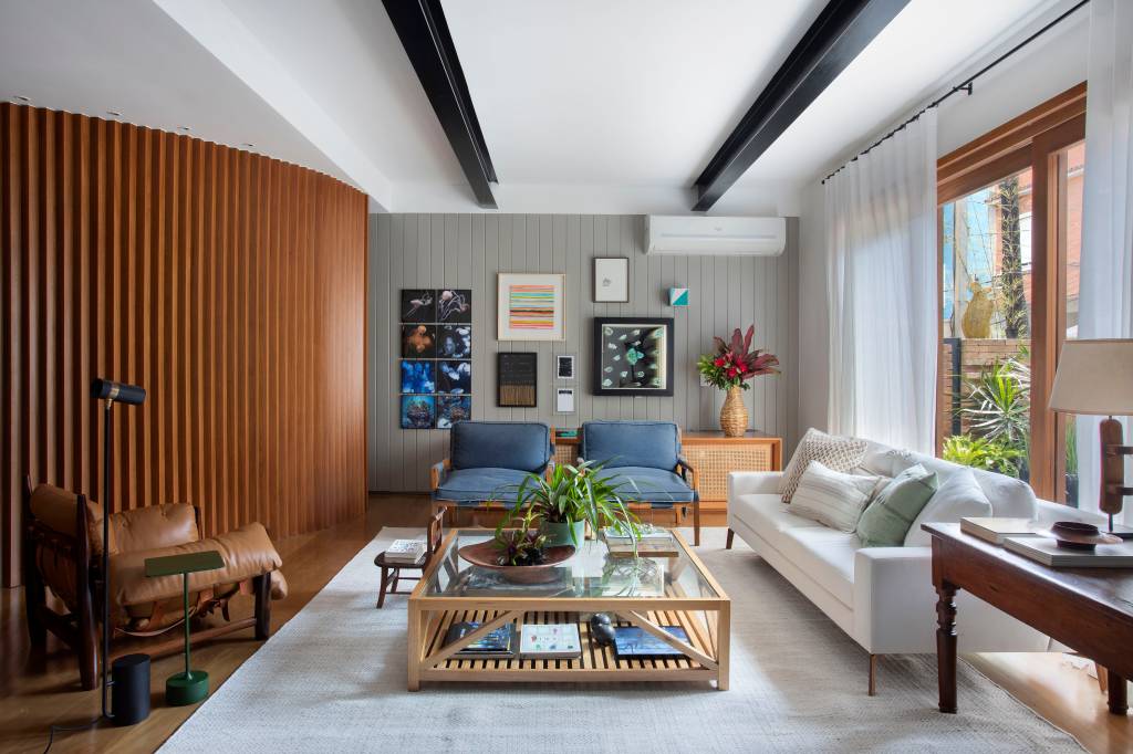 Sala de estar; sofá claro; poltrona azul; tapete; mesa de centro com tampo de vidro; gallery wall; parede de madeira ripada