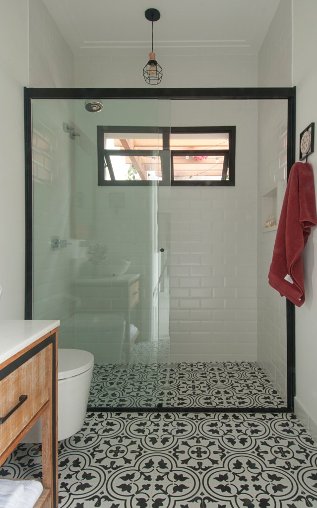 Banheiro com box de vidro e piso de ladrilho hidráulico.