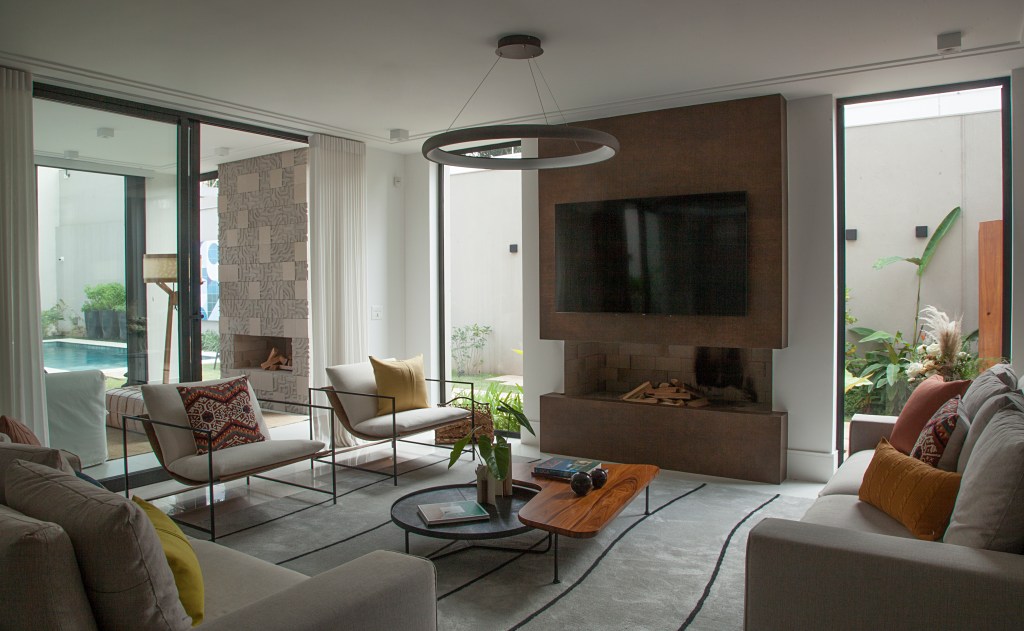 Sala integrada com quintal; sofás claros, poltronas, tv e lustre.