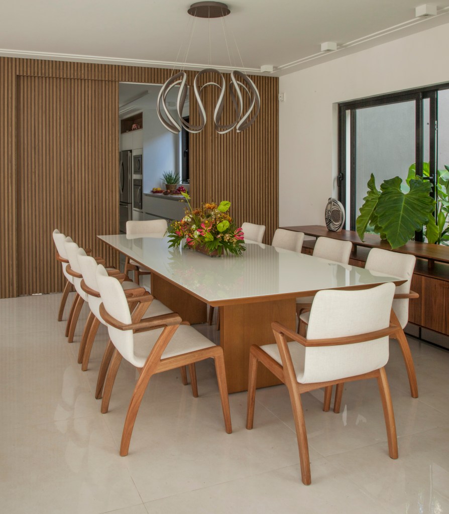 Sala de jantar com piso de porcelanato, mesa com tampo branco, cadeiras estofadas brancas.