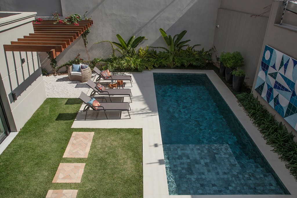 Quintal com jardim e piscina; espreguiçadeiras ao lado da piscina.
