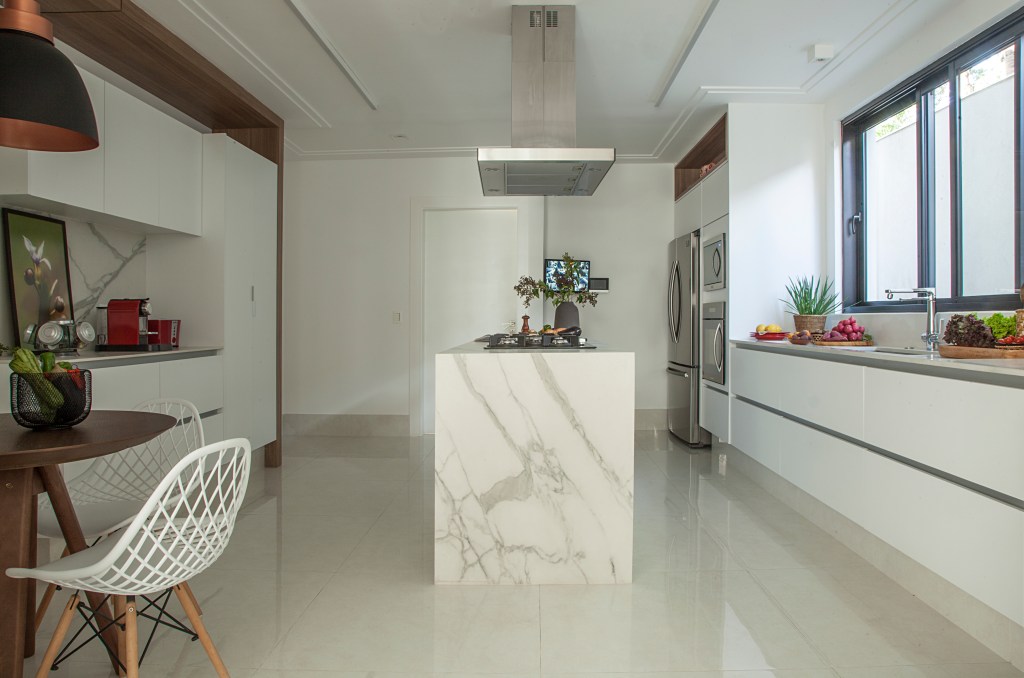 Cozinha branca com ilha revestida de mármore e marcenaria branca.