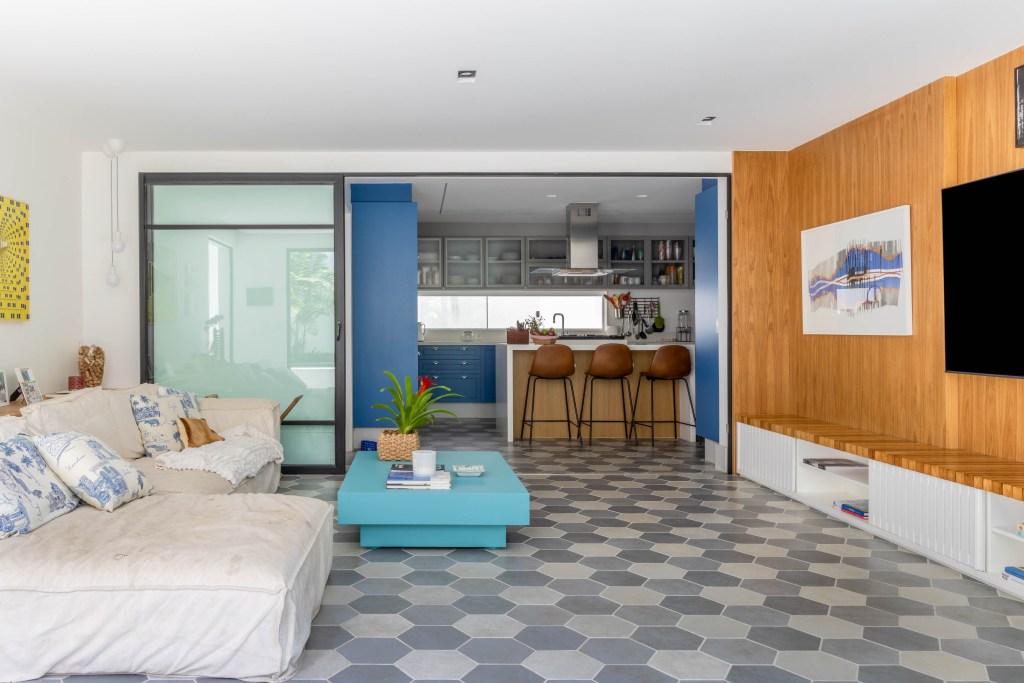 Sala de estar com sofá claro integrada com cozinha; piso geométrico
