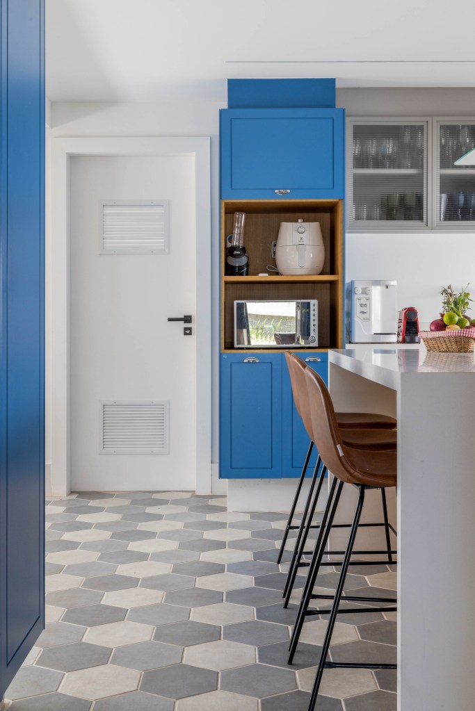 Cozinha com marcenaria azul; ilha de madeira com banquetas; piso geométrico