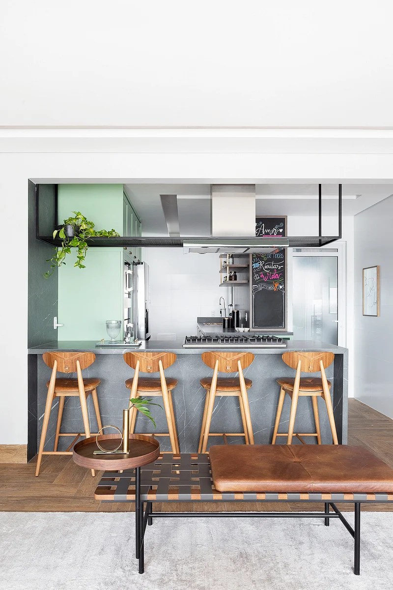 Cozinha integrada pequena; cozinha americana com bancada de quartro lugares e armário verde claro.