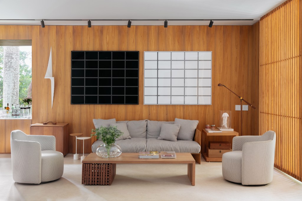 Sala de estar; parede de madeira; sofá cinza; quadro preto e branco; iluminação com trilho de spots; mesa de centro de madeira; tapete off white