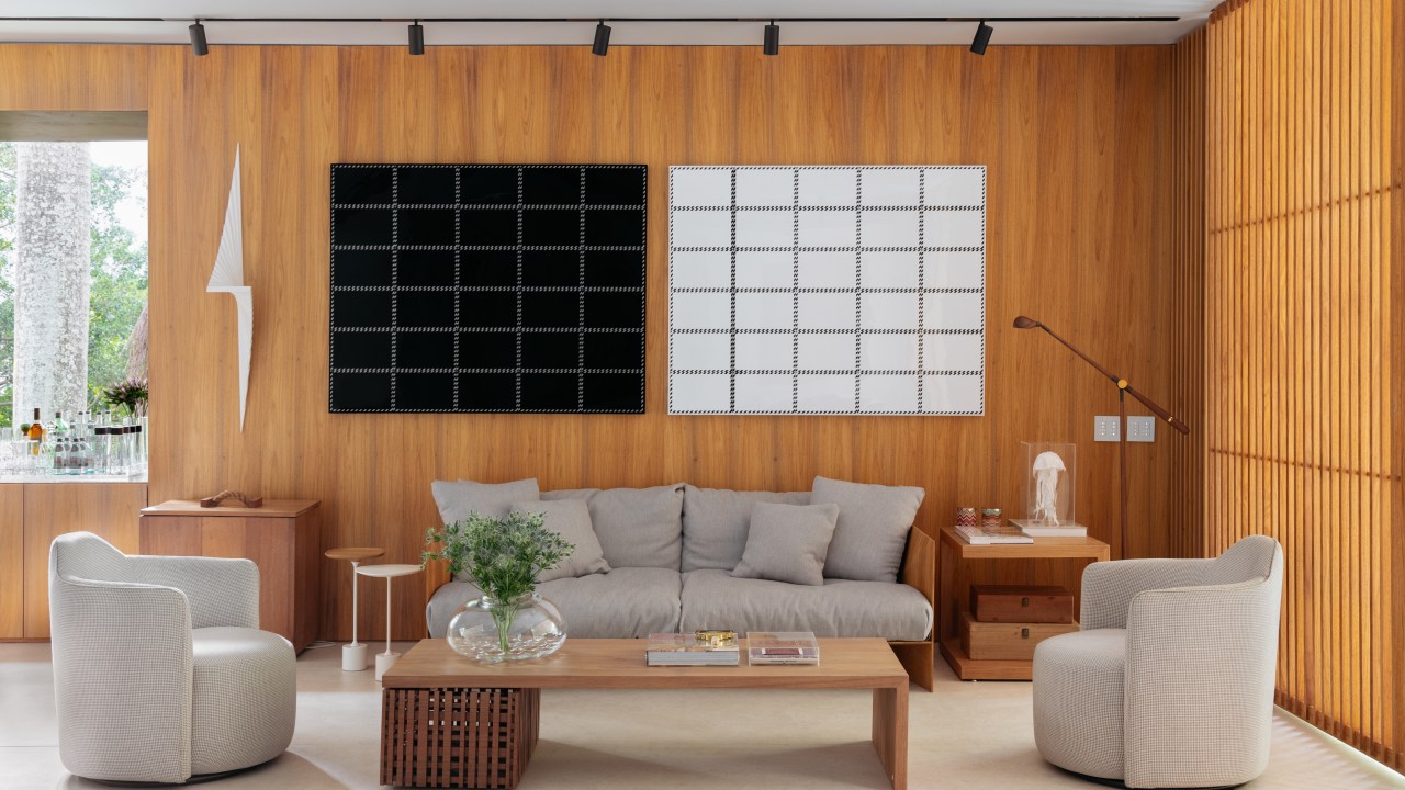 Sala de estar; parede de madeira; sofá cinza; quadro preto e branco; iluminação com trilho de spots; mesa de centro de madeira; tapete off white