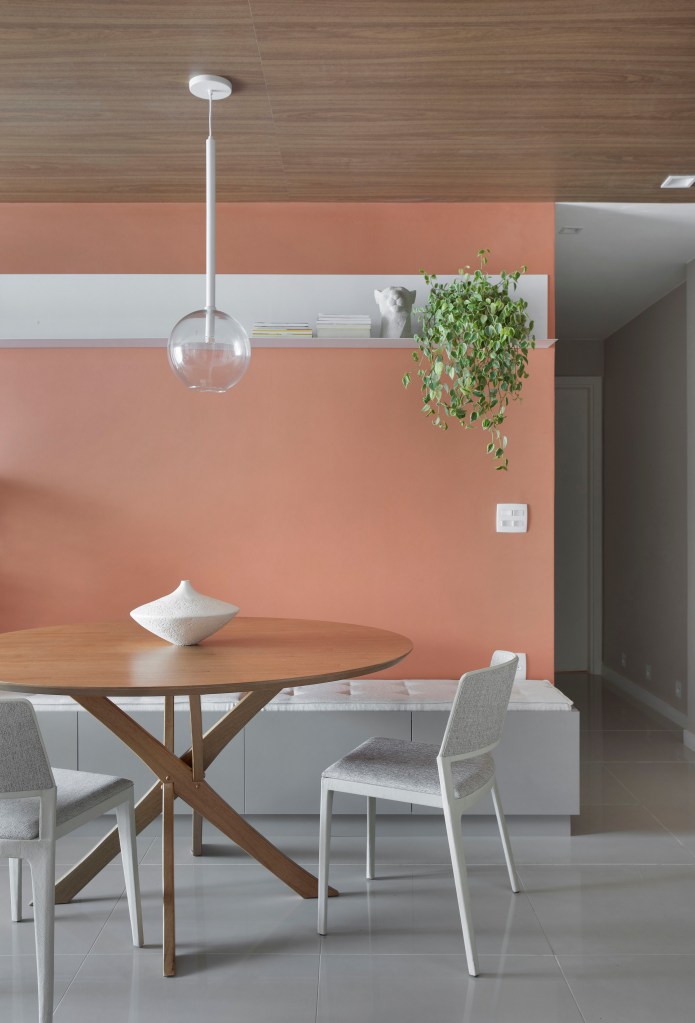 Sala de jantar com parede na cor terracota, mesa de jantar redonda de madeira e cadeiras brancas.